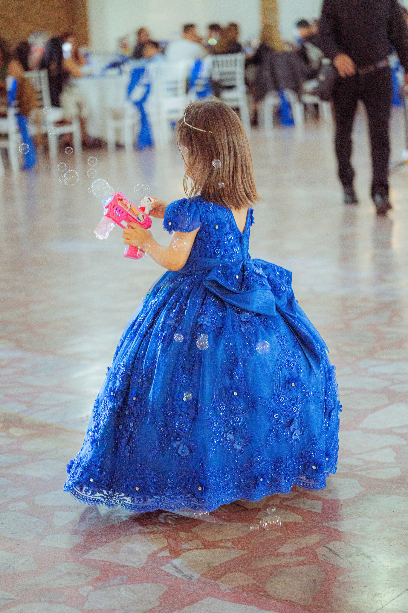 Niña con vestido azul jugando con burbujas en el salón