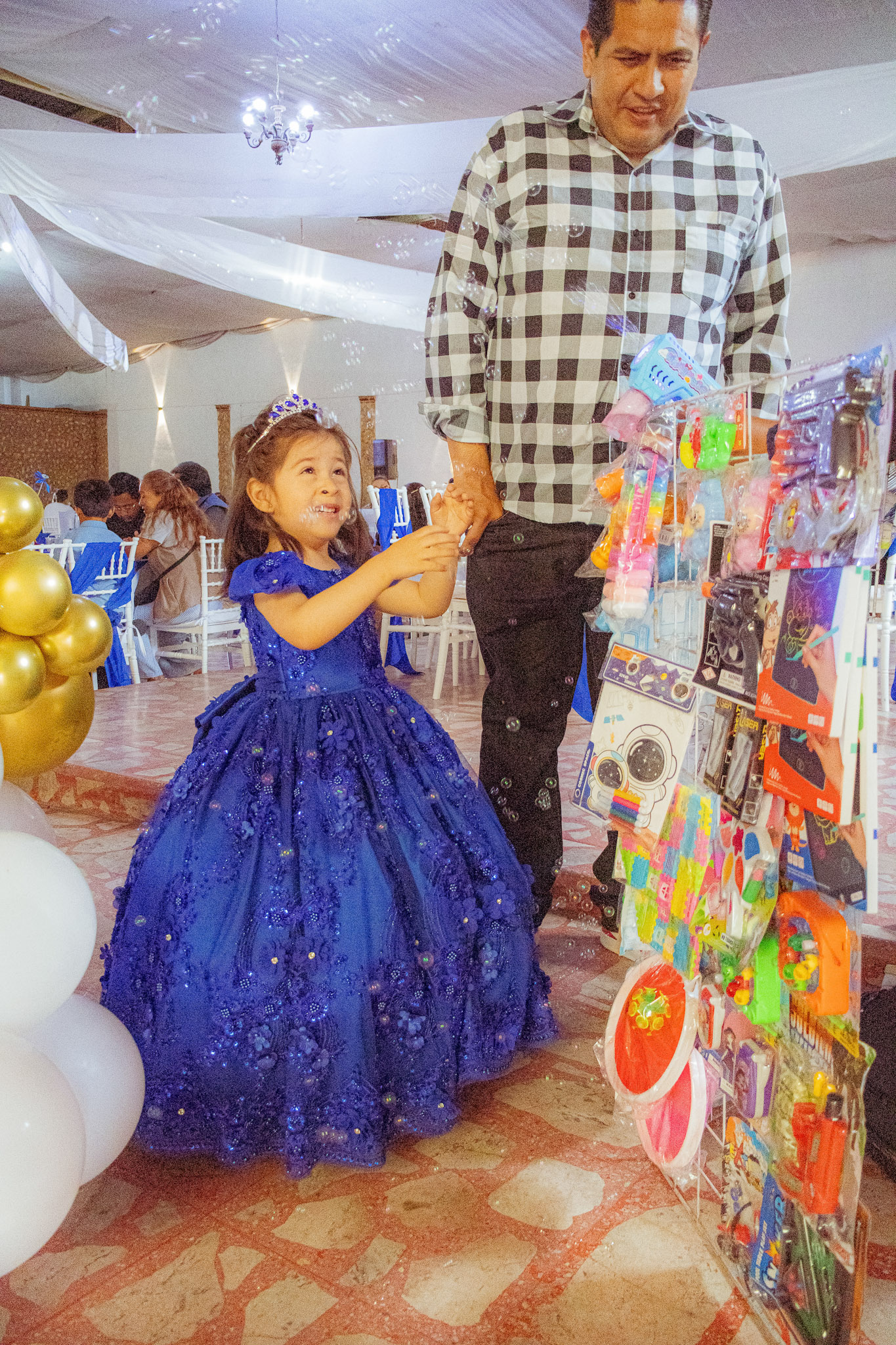 Niña de la mano de su papá junto a la mesa de juguetes